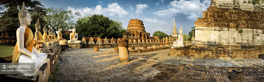 Row of seated Buddha statues and ancient temple ruins.