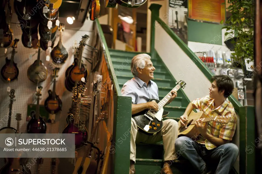 Smiling senior man playing guitar with his teenage grandson.