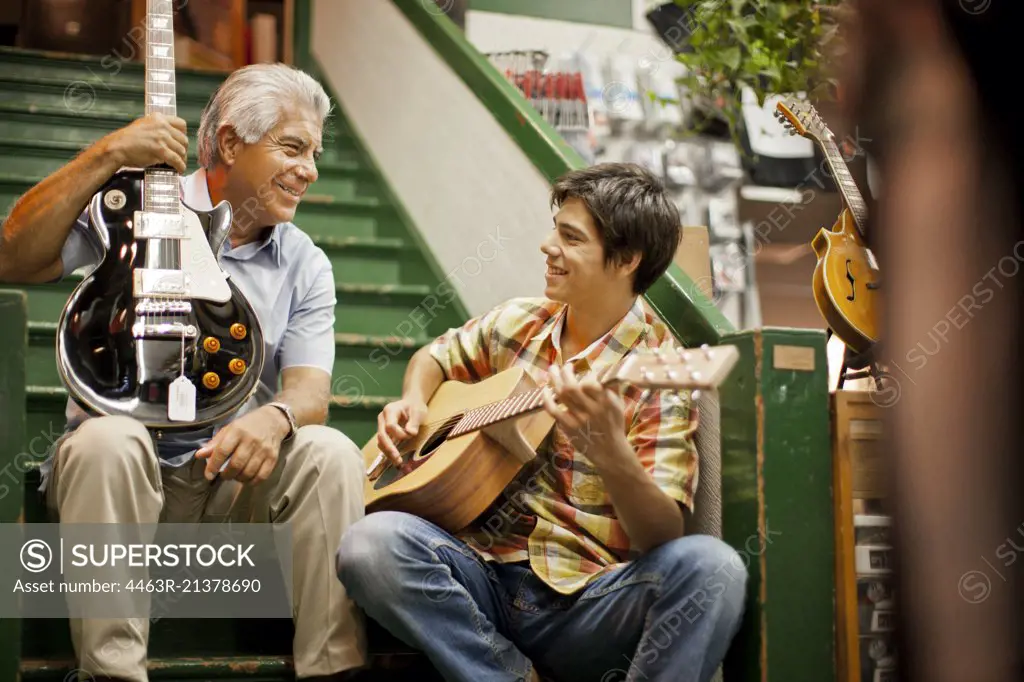 Smiling senior man playing guitar with his teenage grandson.