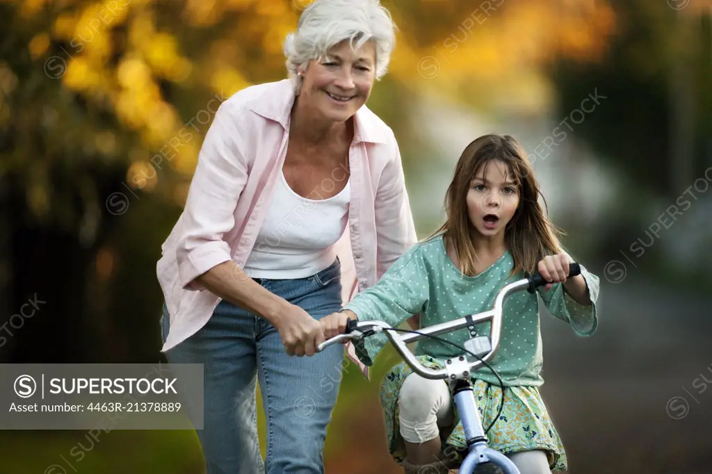 Little girl learning to ride her bicycle with the help of her grandmother.