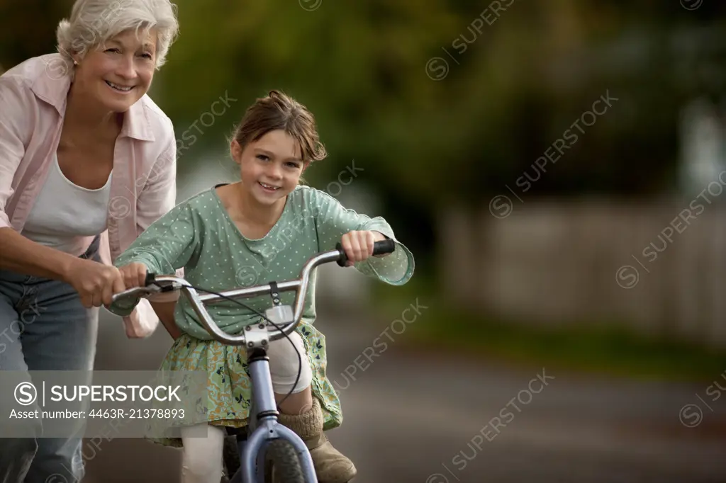 Little girl learning to ride her bicycle with the help of her grandmother.