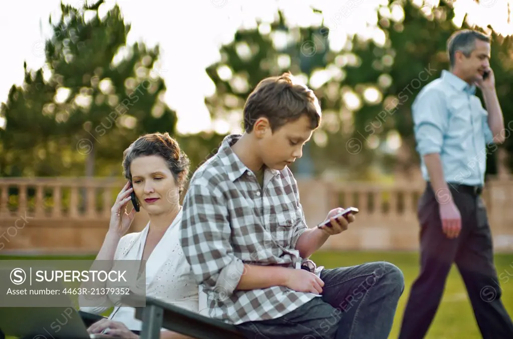 Boy text messaging on his cellphone while his parent are busy on their own cellphones.