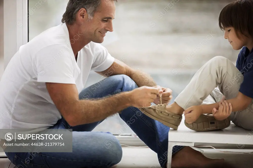 Middle-Aged man helps his young son to tie his shoelaces. 