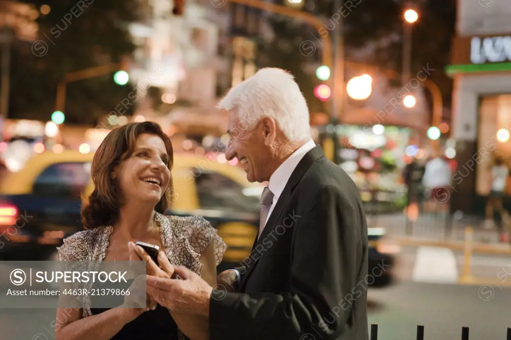 A senior woman smiles as she shows her husband something on her smart phone. 