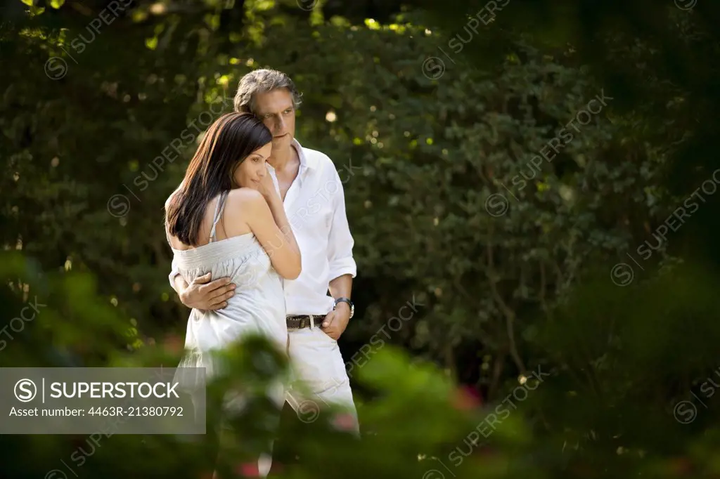 Husband and wife stand in embrace outdoors.