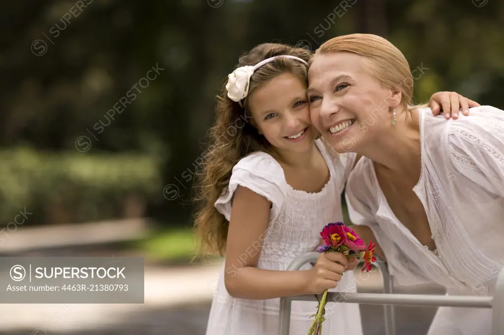 Grandmother and her granddaughter laugh together holding a bunch of flowers.