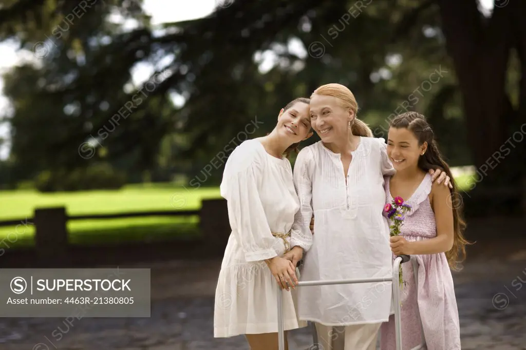 Grandmother, daughter, and granddaughter stand together outdoors at a park.