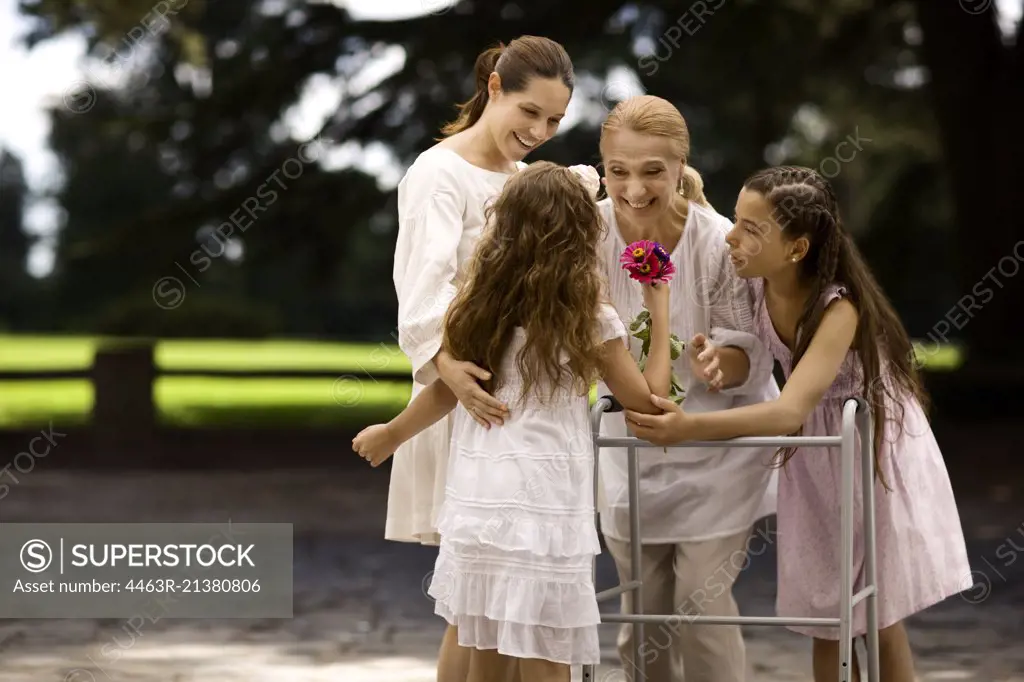 Grandmother and her daughter and granddaughters stand together outdoors as she is presented a bunch of flowers.