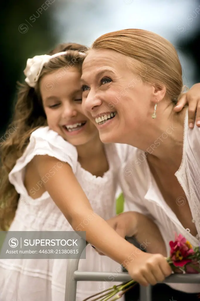 Grandmother and her granddaughter laugh together holding a bunch of flowers.