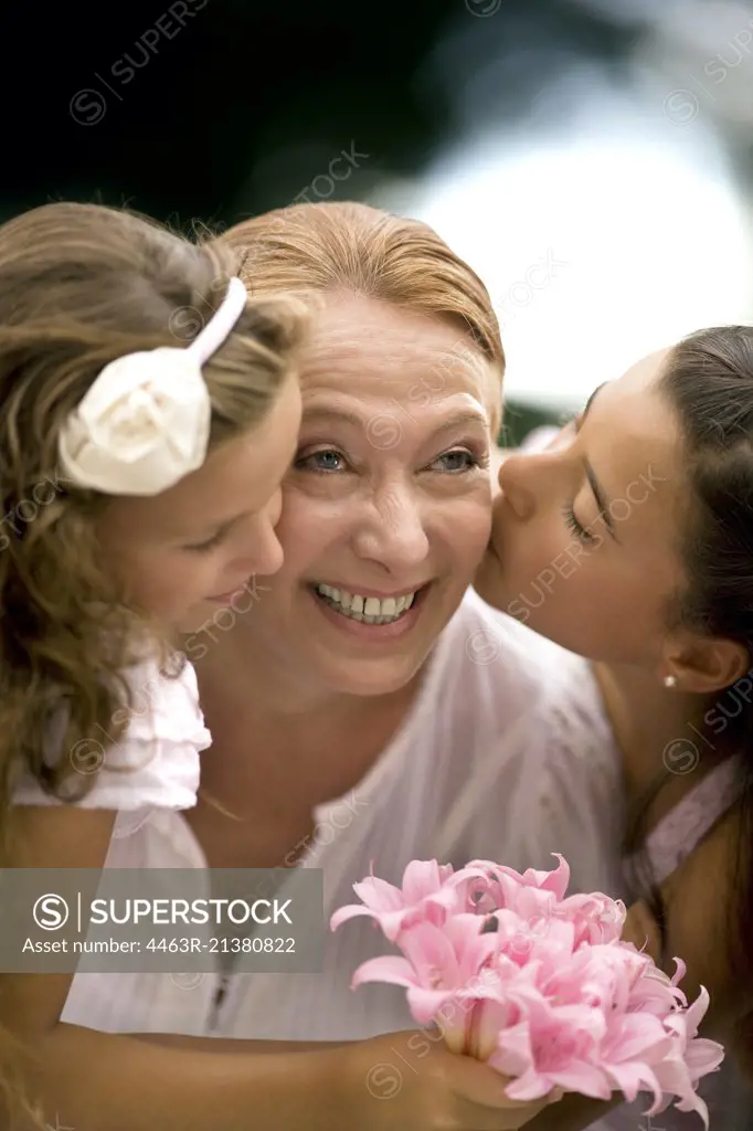 Two young girls kiss their grandmothers' cheeks.