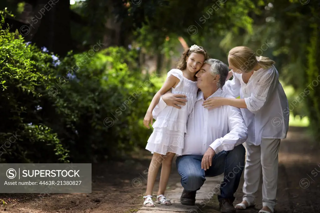 Grandparents stand with their granddaughter on a quiet country road.