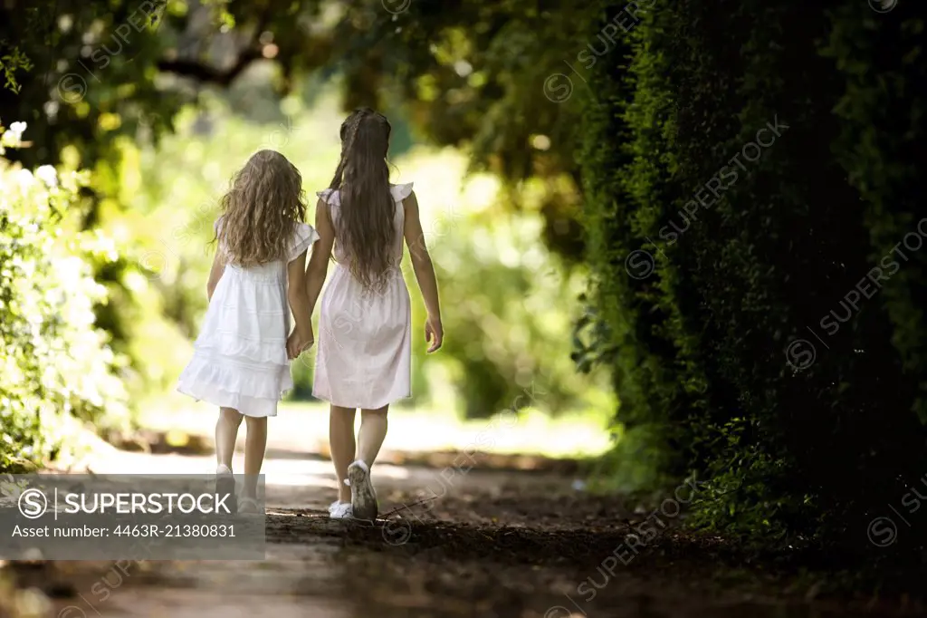 Two young girls hold hands and walk down a quiet country road.