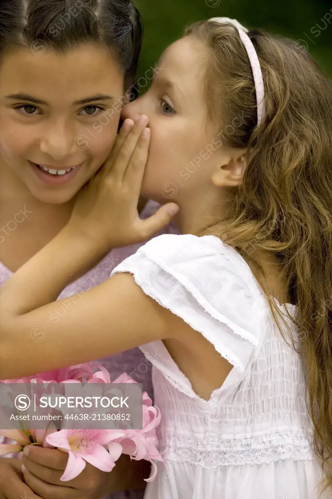 Young girl whispers in her sisters ear.