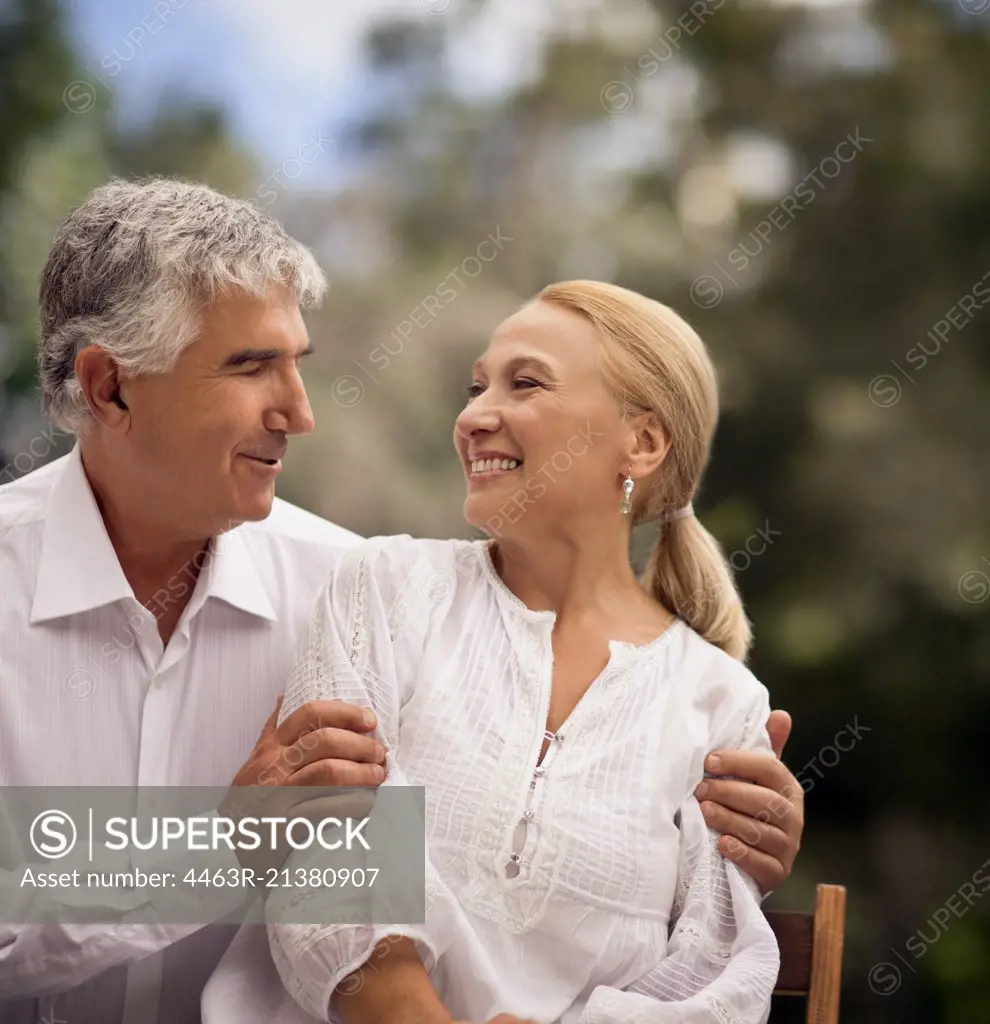 Elderly couple look into each others eyes while sitting outdoors.