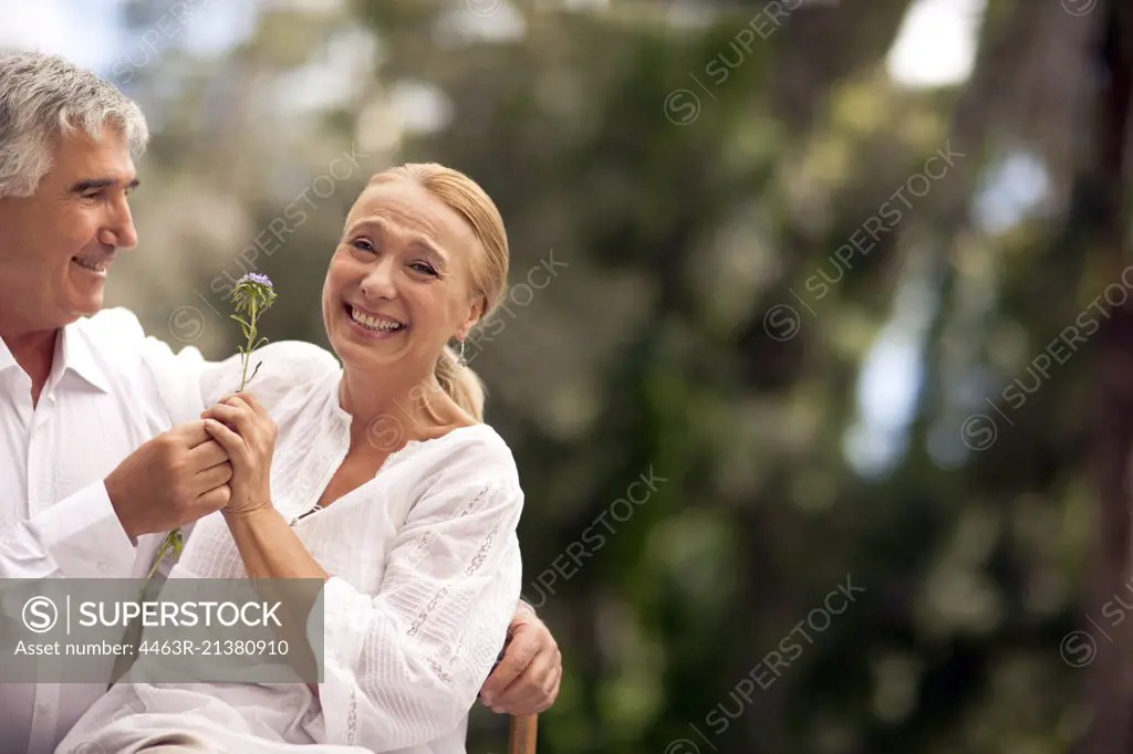 Husband gives his wife a flower as they sit outdoors.