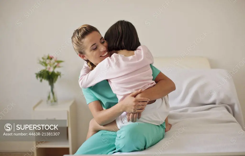 Young girl hugging nurse in hospital room.