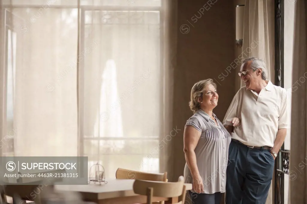 Happy mature couple standing in dining room. 