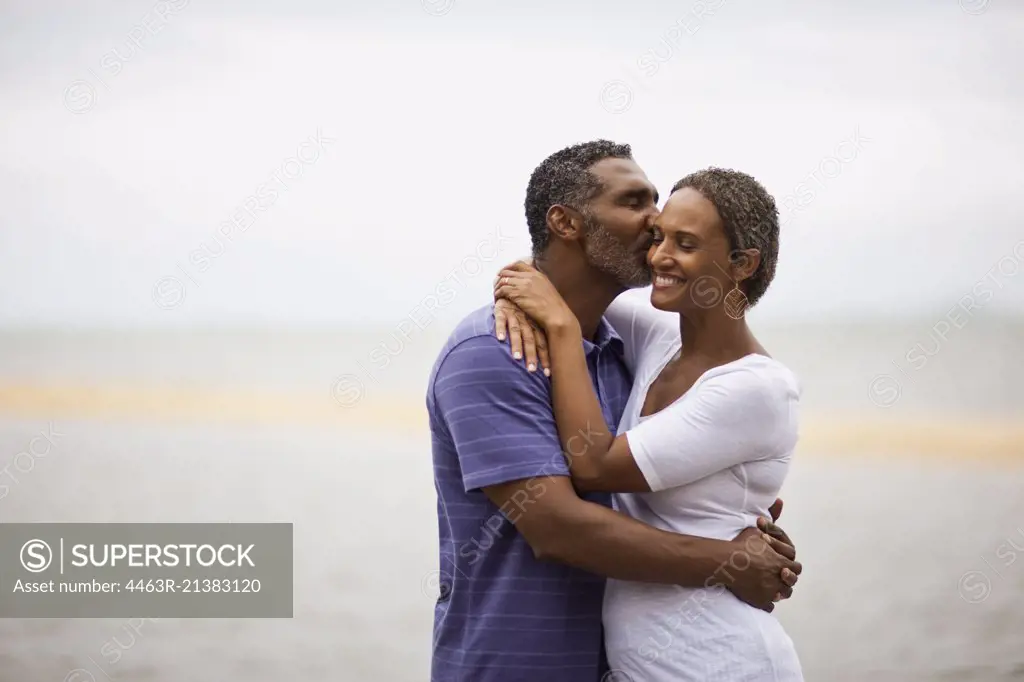 Mature man kissing his wife on the beach.