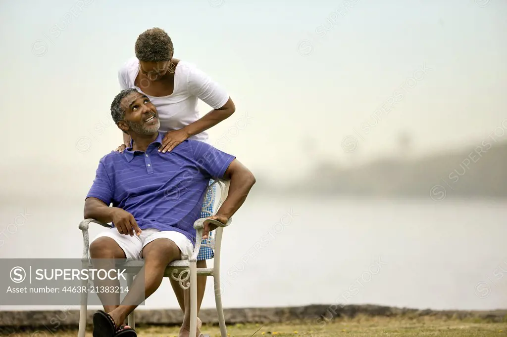 Mature man receiving shoulder massage from his wife by the beach.