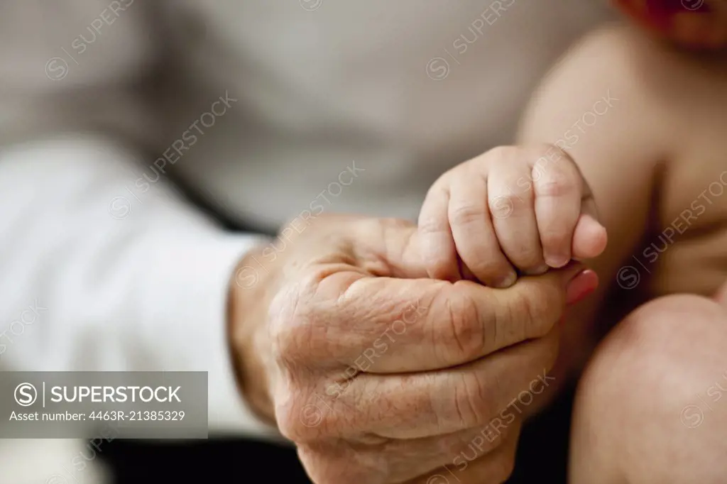 Close-up of elderly woman's hand as she holds her baby grandson's hand.