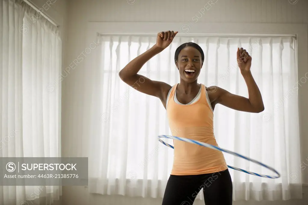 Portrait of a happy young woman hula hooping in her living room.