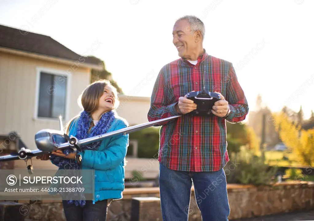 Smiling girl and her grandfather having fun playing with a toy airplane together in the back yard.