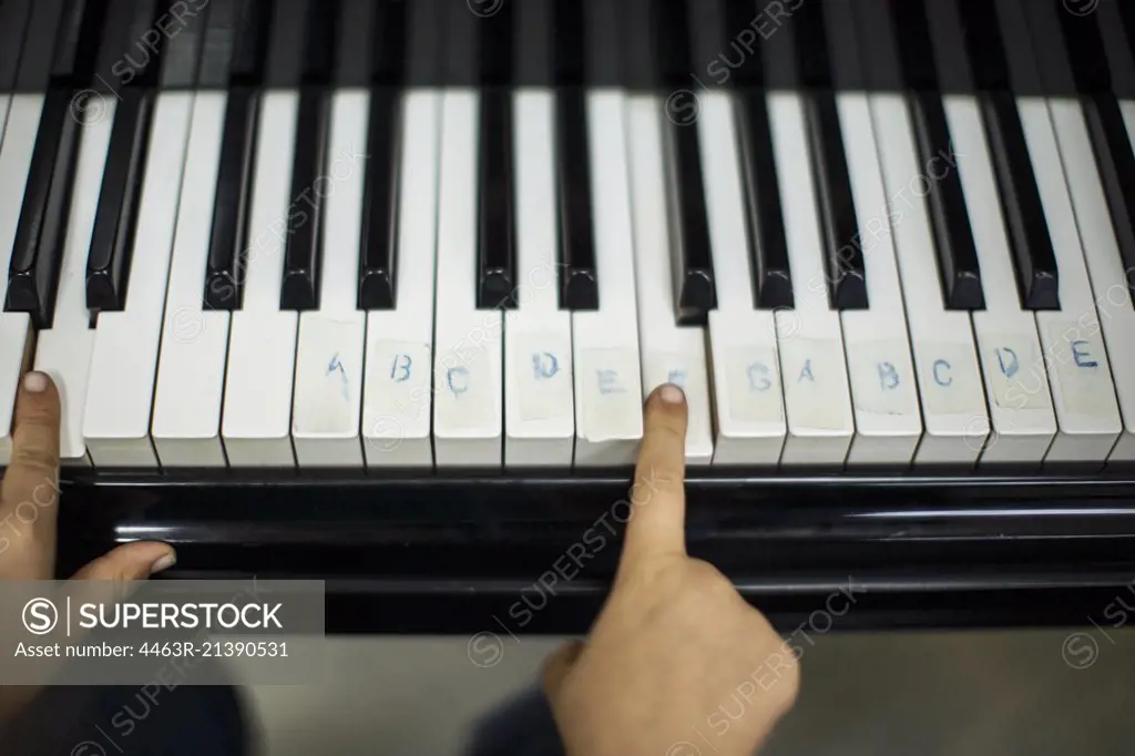 Young boy learning to play the piano helped by notes taped to the keys.