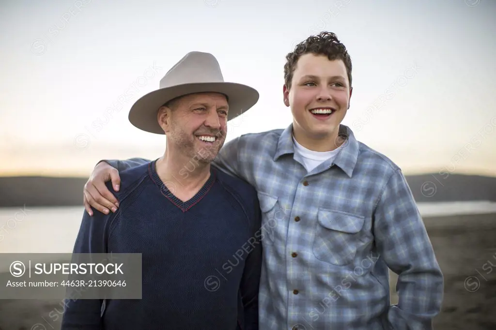 Teenage boy and his dad laughing together on the beach at sunset.