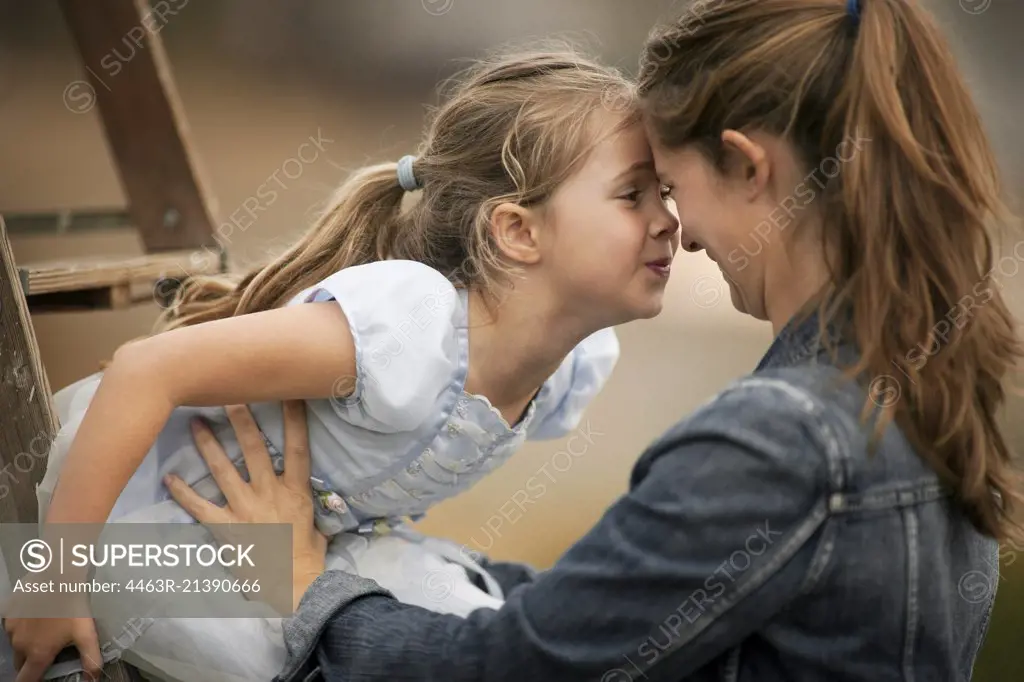 Smiling young mother holds her little girl who is sitting on a ladder.