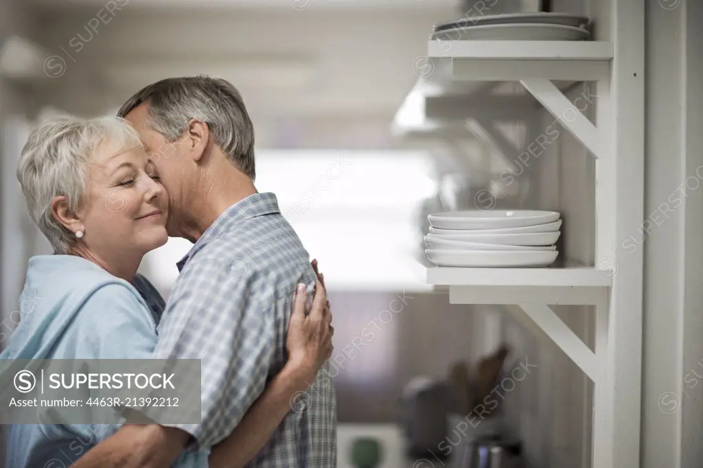 Affectionate mature couple tenderly embrace in the kitchen.