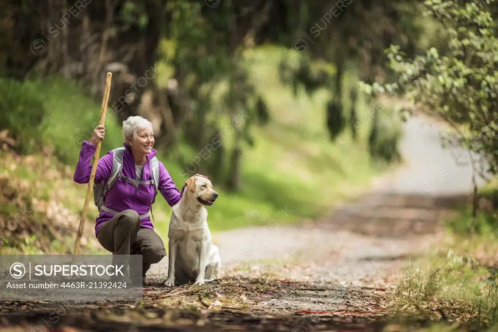 Portrait of a cheerful mature woman taking a break from hiking in the forest to pet her dog.