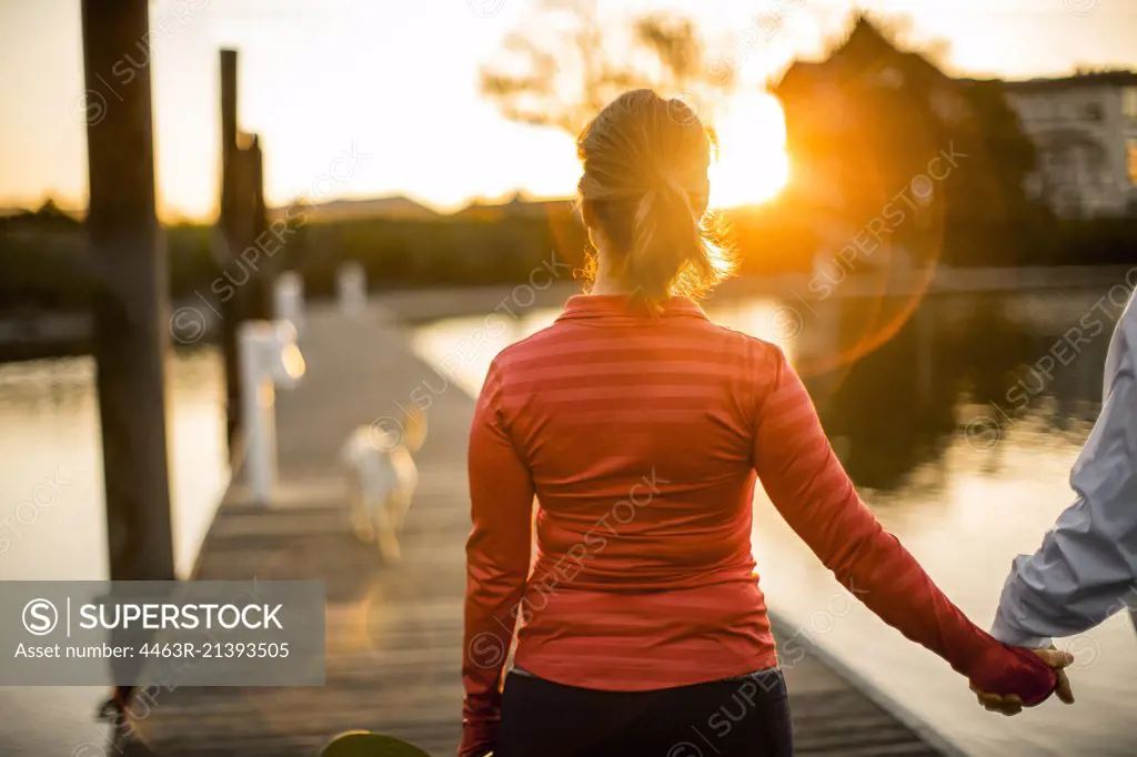 Couple walking hand in hand along a pier at sunset.