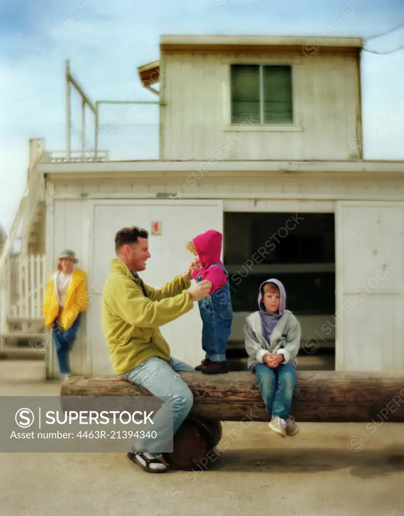 Side view of a father playing with his kids in front of a house.