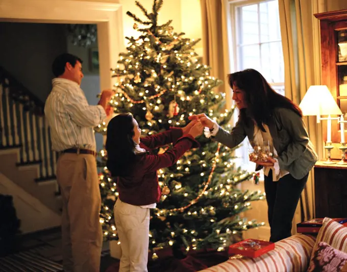 Girl decorating Christmas tree with parents