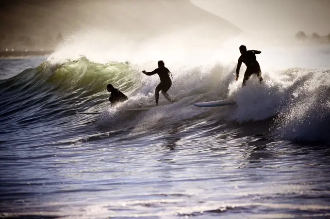 Three people surfboarding on the crest of a wave.