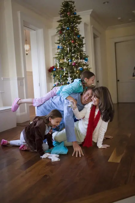 Happy family playing together next to the Christmas tree inside their home.