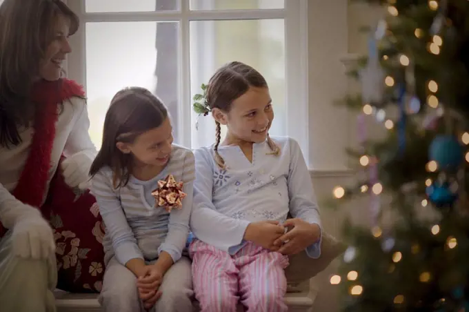 Two smiling young sisters and their mother sitting side by side on Christmas day.