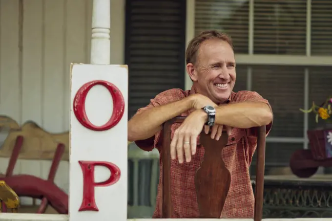 Smiling mature store owner relaxes on the veranda of his antiques shop.