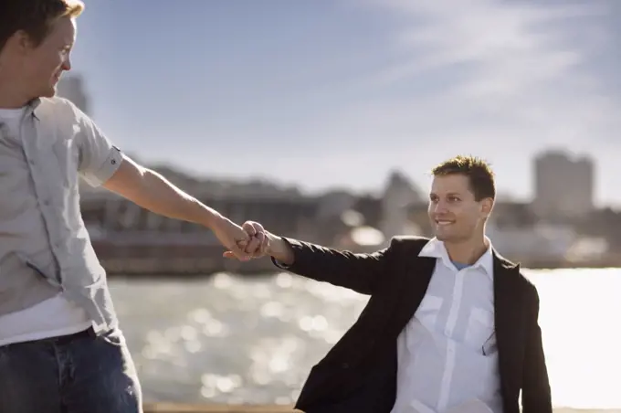 Two young homosexual men looking at each other while holding hands.