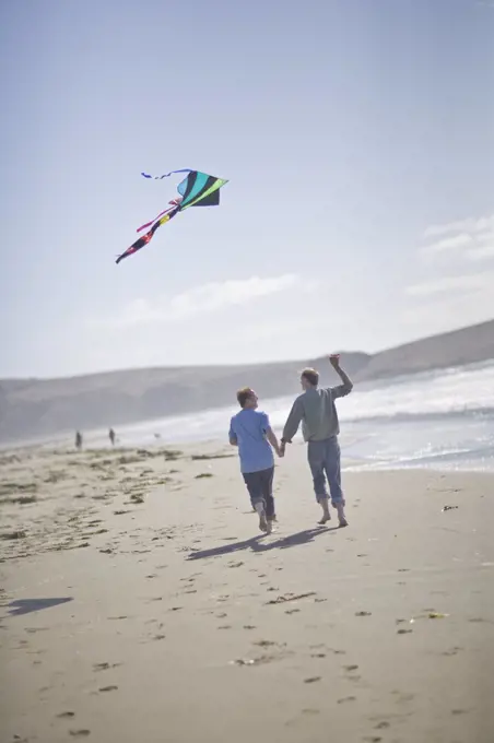 Happy male couple flying a kite while holding hands on a beach.