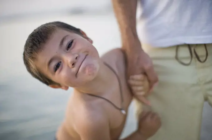 Portrait of a young boy smiling while holding his dads hand.