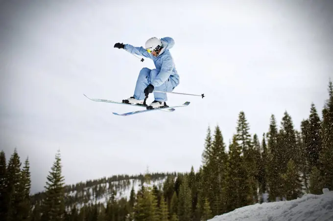 Young man jumping mid-air while riding his skis outdoors in the snow.