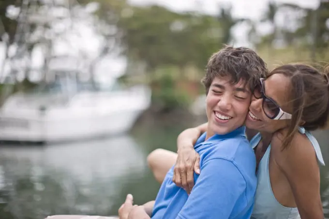 Smiling mother hugging her teenage son from behind.