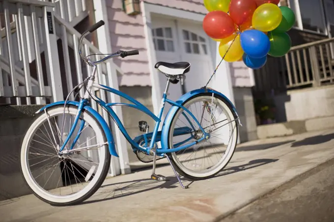 Blue bicycle with bunch of colorful balloons tied to it.