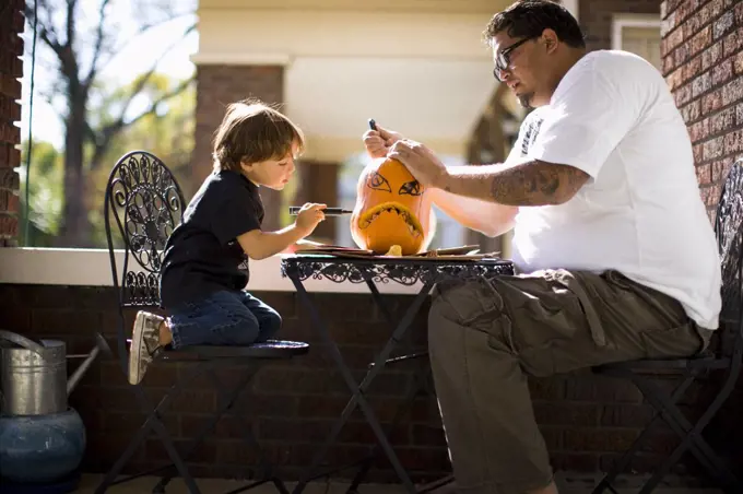 Father and son drawing face on pumpkin and carving Jack O' Lantern