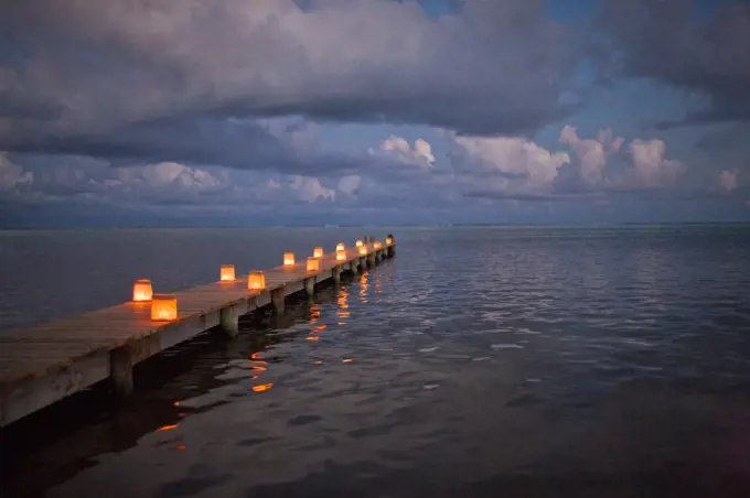 Tropical ocean pier lit by glowing paper lanterns at twilight.