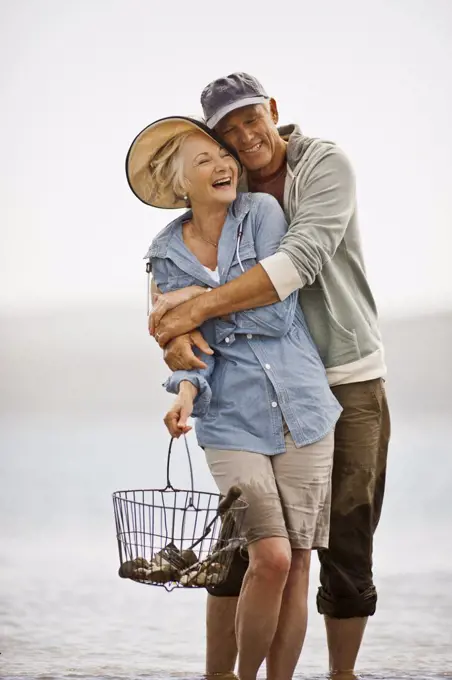 Smiling senior couple wading on a beach at low tide.