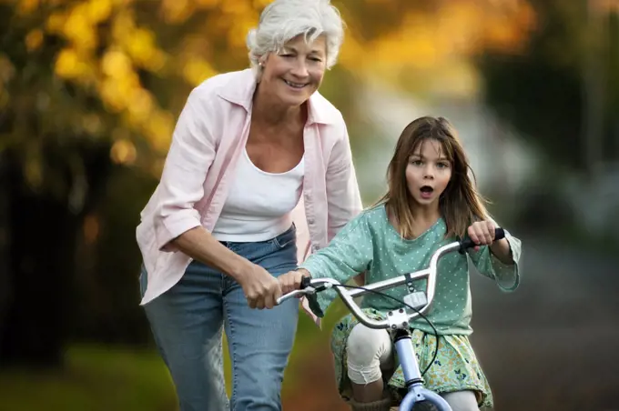 Little girl learning to ride her bicycle with the help of her grandmother.