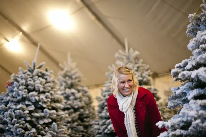 Woman playing hide and seek at a Christmas tree lot.