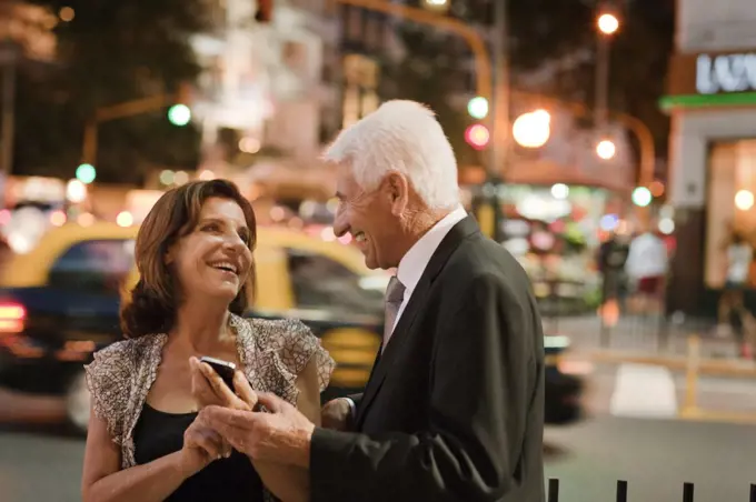 A senior woman smiles as she shows her husband something on her smart phone. 